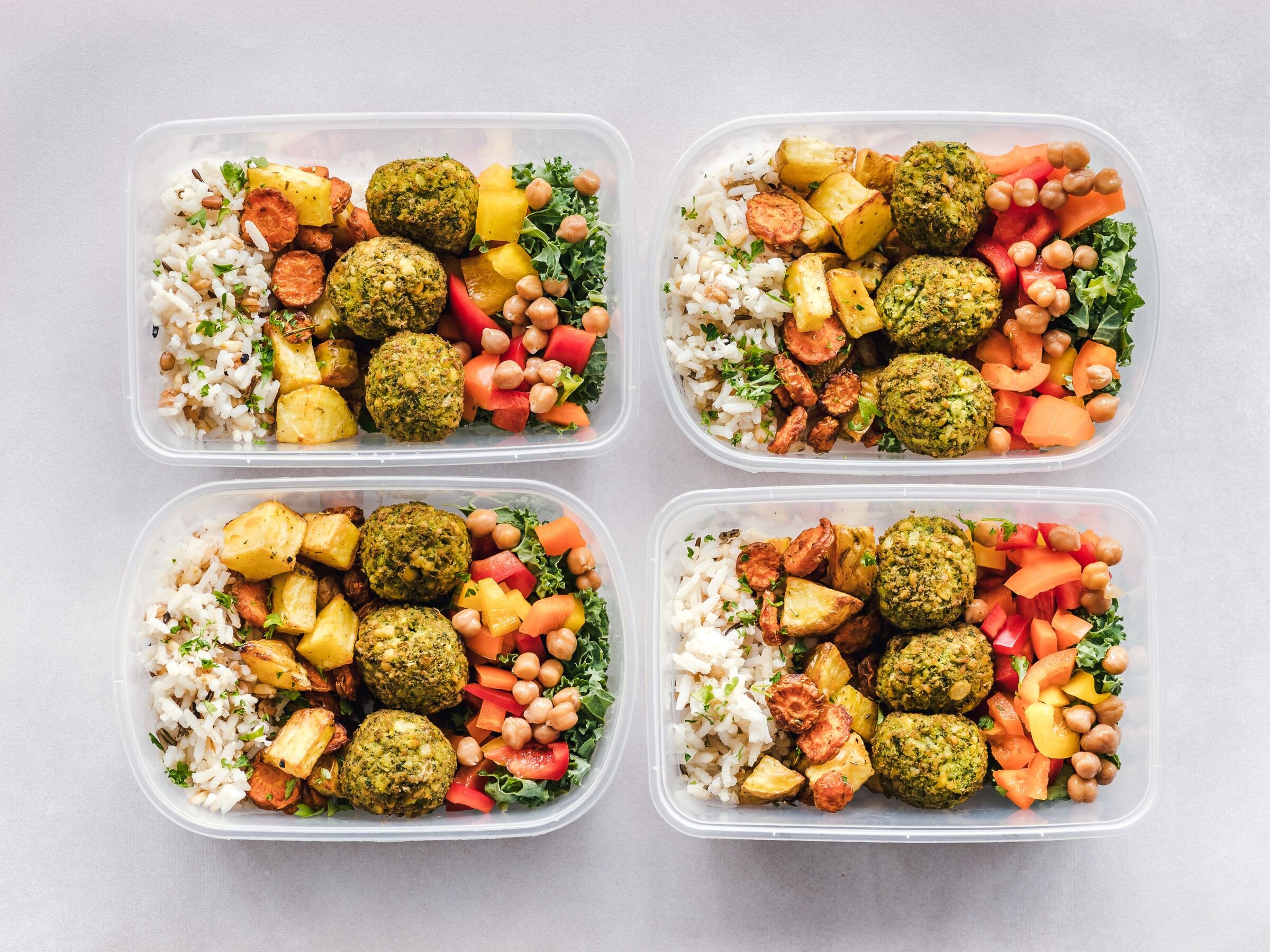 Four meal-prep boxes of grains, roasted vegetables and falafel