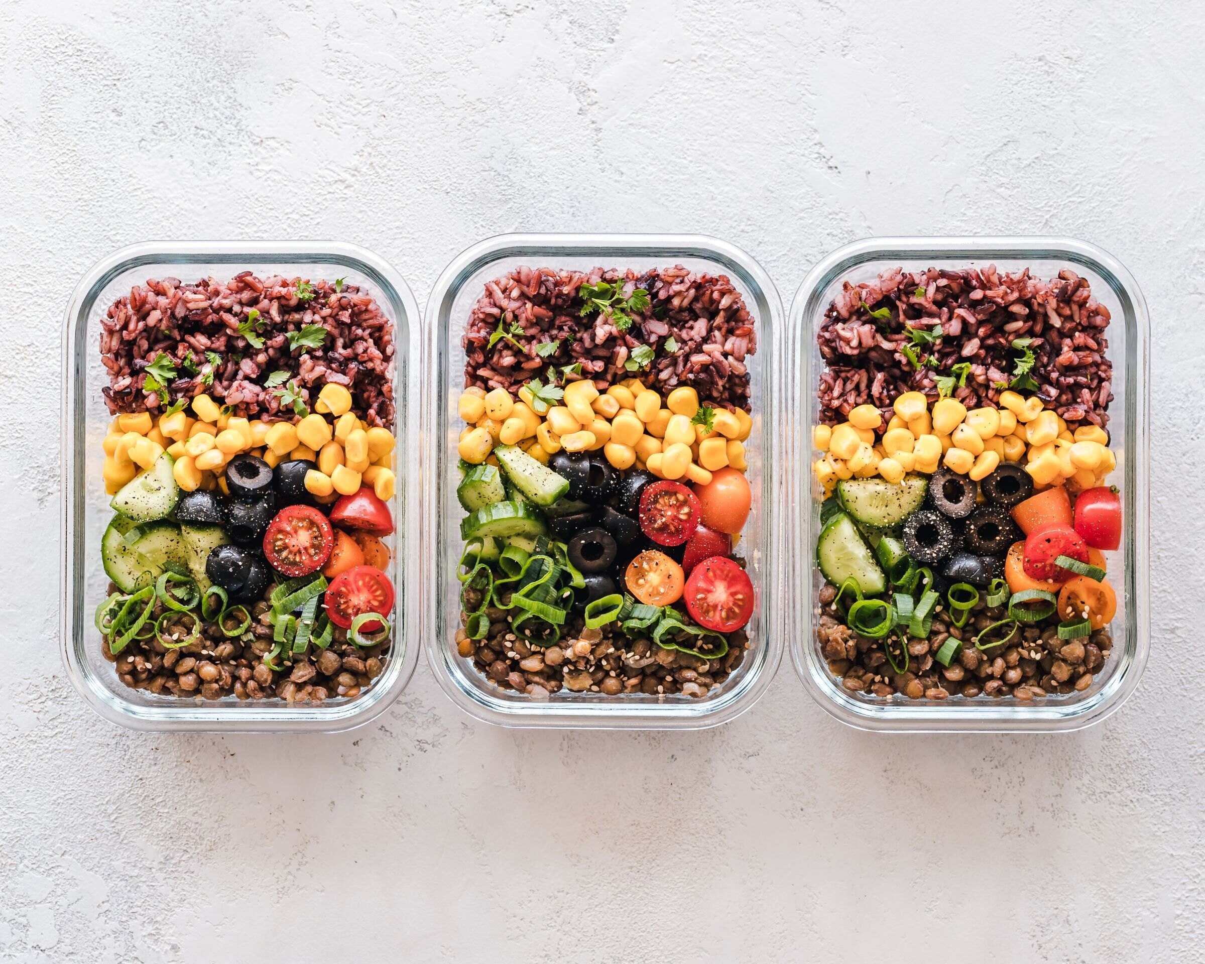 Three meal-prep boxes of grains, corn, olives, tomatoes and cucumber